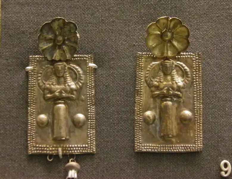 An angel-like figure and a flower on a piece of gold jewelry